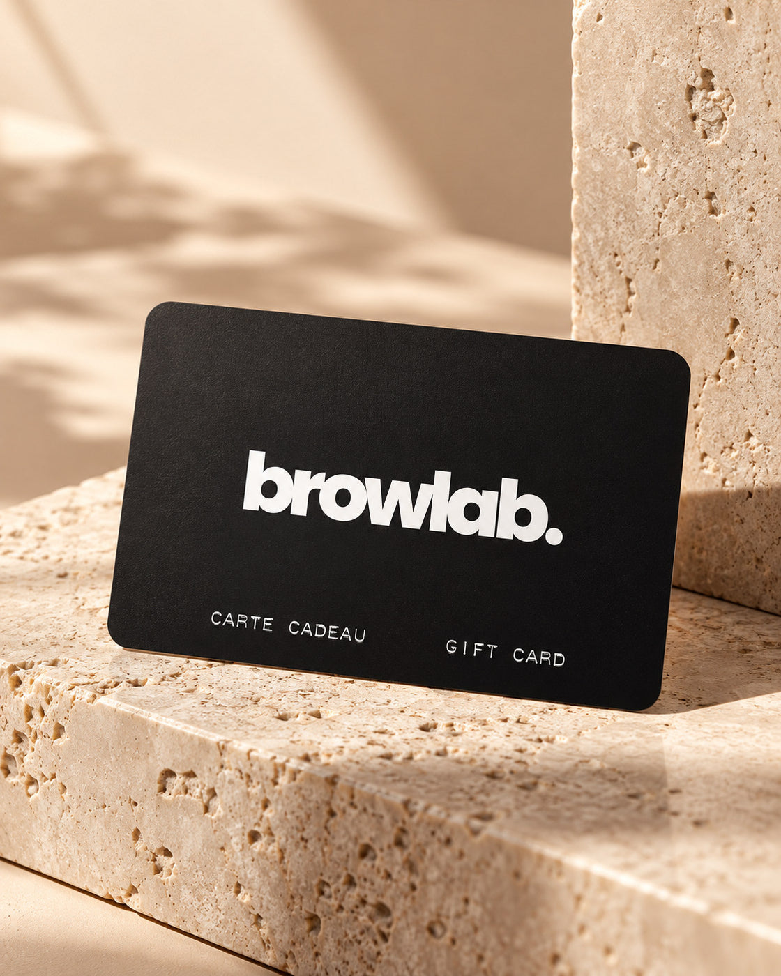 Détail rapproché de la carte cadeau Browlab noire sur travertin beige